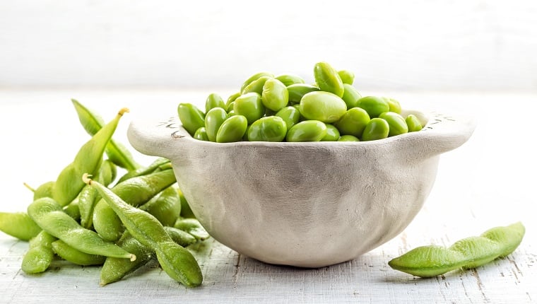 A bowl of green beans on a white wooden table