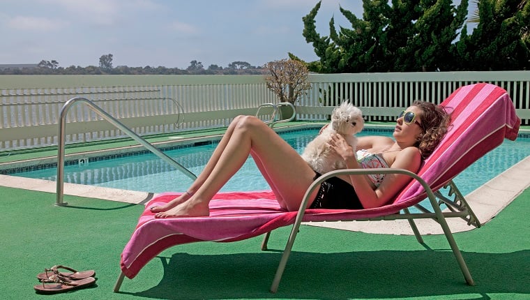 Woman lying on a sundeck chair by the pool with a dog on her belly